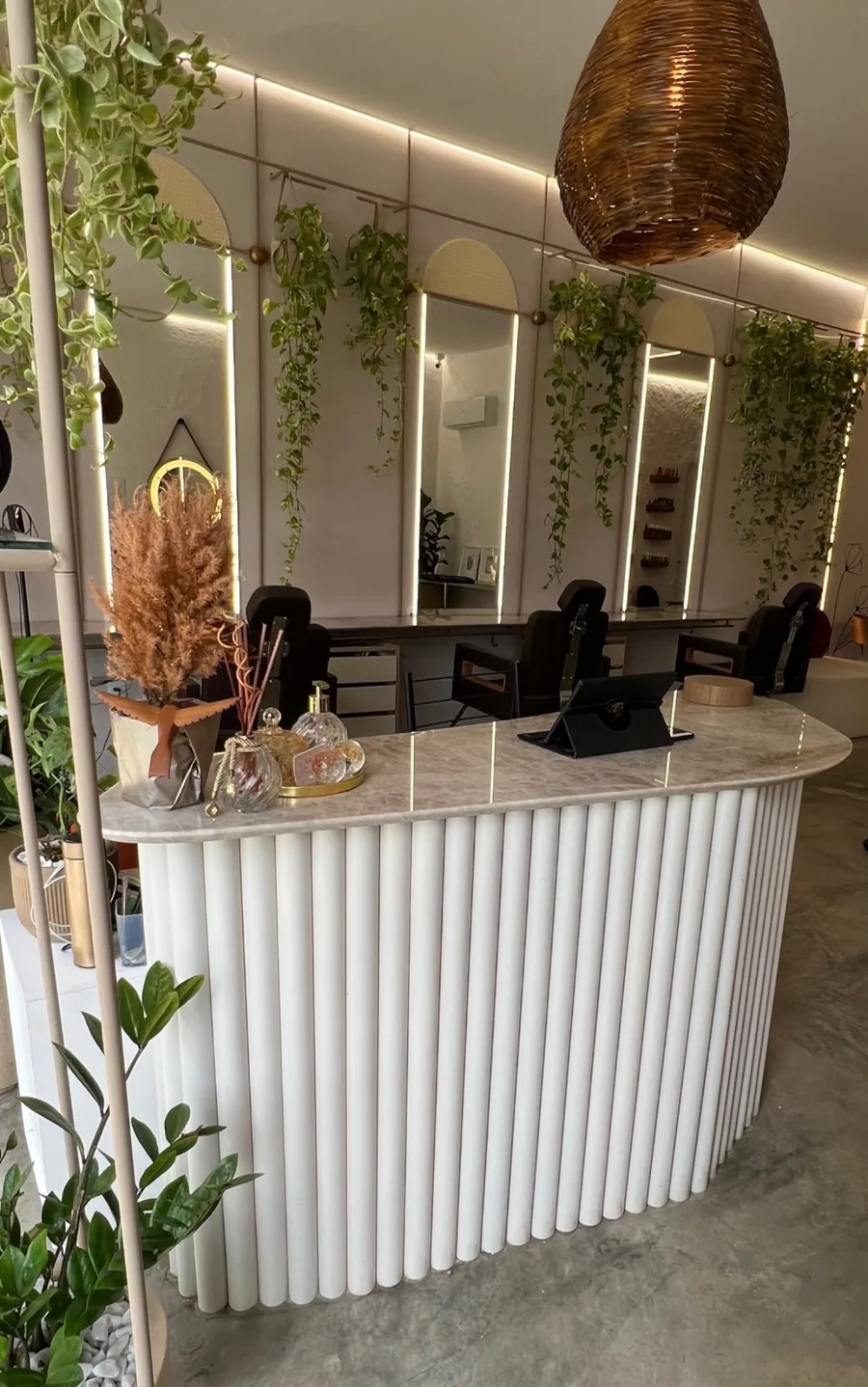 Bancadas do Beleziara com espelhos arqueados, plantas pendentes e balcão canelado