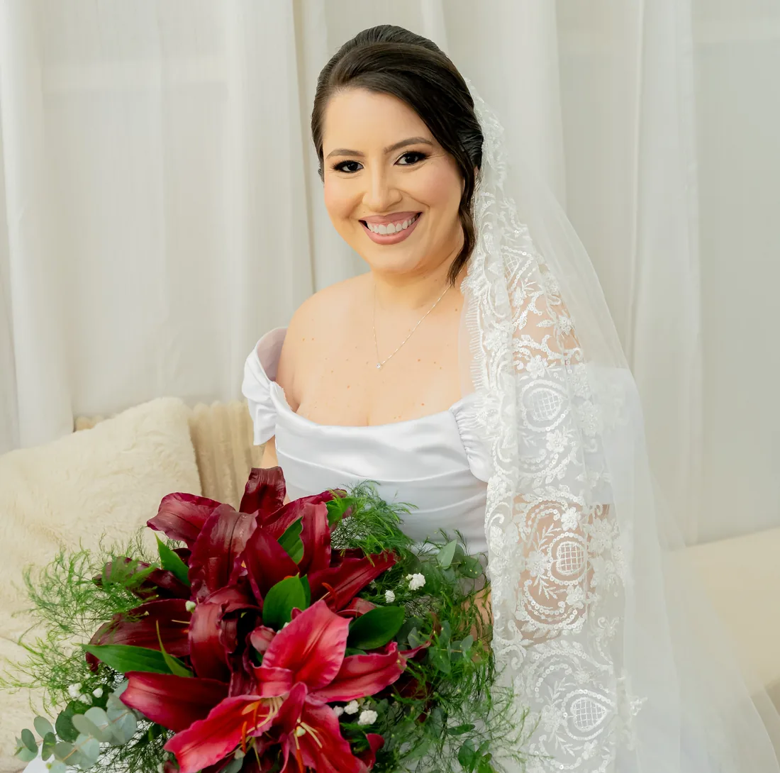 Noiva Iasmine com véu de renda e buquê de lírios vermelhos